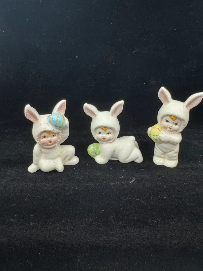 Set of three vintage ceramic baby figurines in bunny costumes holding Easter eggs