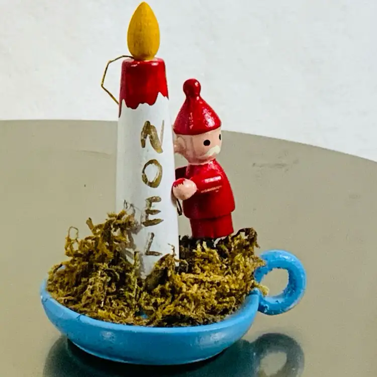 Handmade Wooden Boy Santa Wearing All Red  Positioning A Noel Candle On top Of A Blue Candlestick Holder Vintage Christmas Ornament Approximately 2” Tall And 2.5” Long