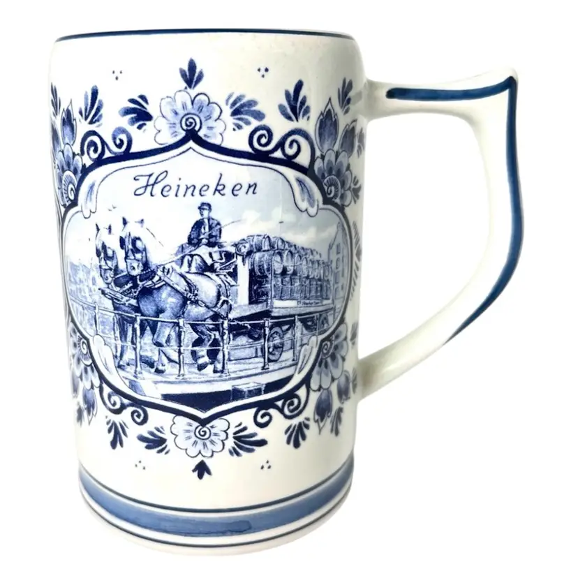 Heineken Ceramic Stein Mug. Holland Delft Blue & White. Draft Horses Pulling Beer Keg Cart & Dutch Windmill Images. Signed On Bottom. 5-1/4” tall x 5” across top mouth-to- handle x 3-1/2” diameter across bottom.