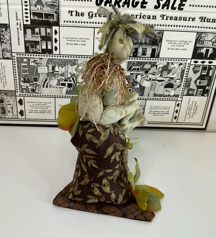 Forest Witch made of green and brown fabric, ribbon, silk flowers sitting on her house, hand painted face. Signed and dated 2004, 9” tall and 5 1/2” across base