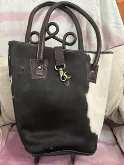 This is a black and white hair-on-hide cowhide Shoulder bag with dark brown rolled leather handles and a brass closure.