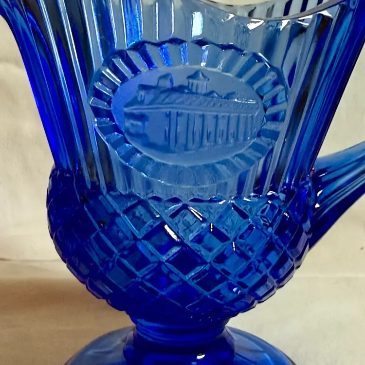 Vintage 1976 Avon Fostoria cobalt blue glass pitcher featuring an embossed image of Mount Vernon, George Washington's home.