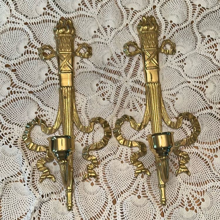 Vintage brass wall sconce Pair, often referred to as a "torch and ribbon" style candle holder. These were made by The Bombay Company, dated 1992. Elevate your home decor with these stunning vintage Bombay brass wall sconces. The intricate carvings and antique brass finish add a touch of Hollywood Regency style to any room.