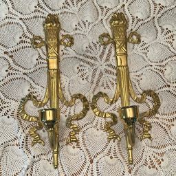 Vintage brass wall sconce Pair, often referred to as a "torch and ribbon" style candle holder. These were made by The Bombay Company, dated 1992. Elevate your home decor with these stunning vintage Bombay brass wall sconces. The intricate carvings and antique brass finish add a touch of Hollywood Regency style to any room.