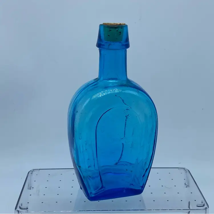 #0230 Decorative blue glass bottle with a horseshoe motif made in Taiwan 7” x 3” Flaw