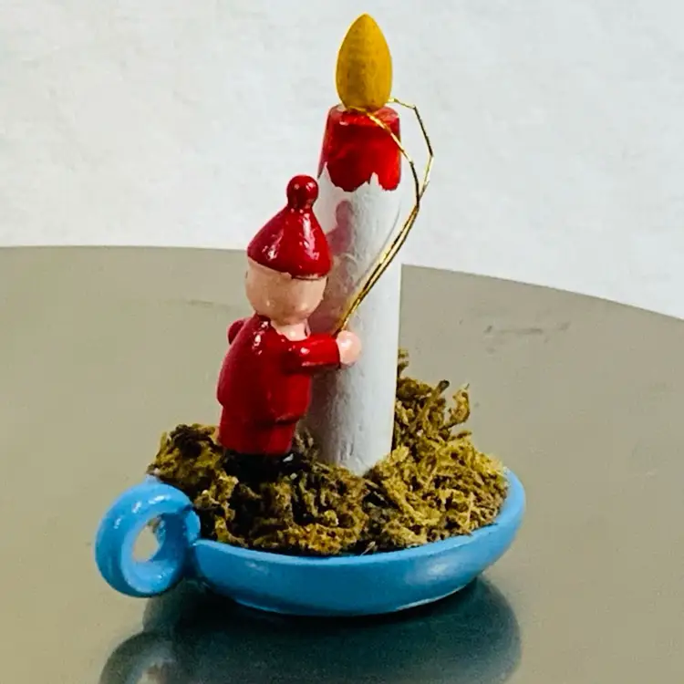 Handmade Wooden Boy Santa Wearing All Red  Positioning A Noel Candle On top Of A Blue Candlestick Holder Vintage Christmas Ornament Approximately 2” Tall And 2.5” Long