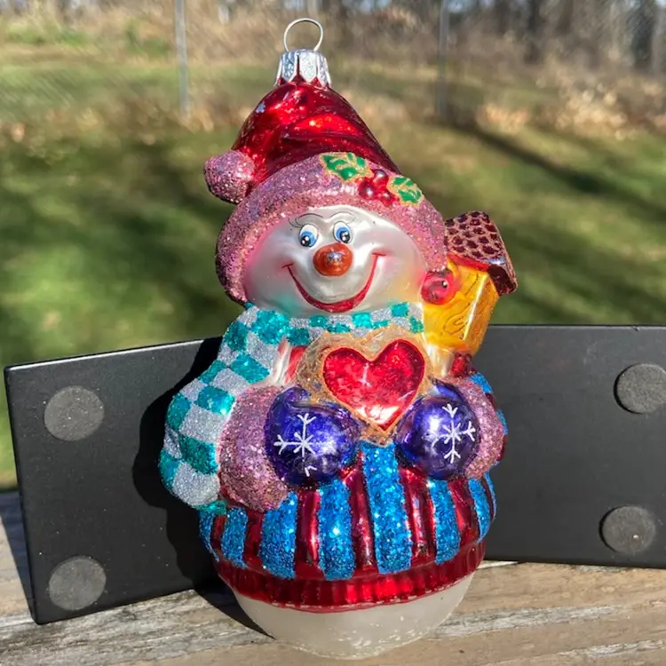 Blown Glass Snowman Christmas Ornament. Purple Mittens Holding Red Heart With Gift On Shoulder. Red Hat & Green And Silver Checkered Scarf. Attached Hanger. 5.5”h x 3”w.