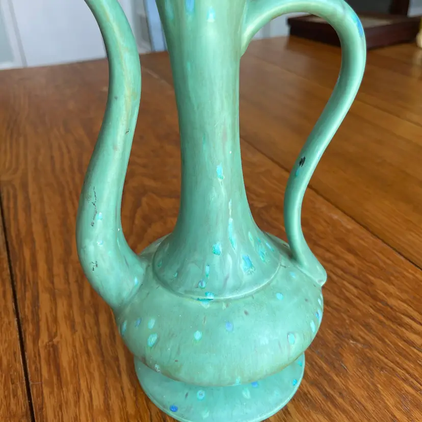 A speckled green ceramic pitcher with a curved handle and slender spout. Circa 1970- No Stopper 9.5”