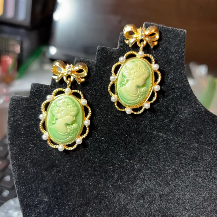 Exquisite vintage-inspired green cameo earrings featuring gold tone studs embellished with faux pearls and clear gemstones on the bow