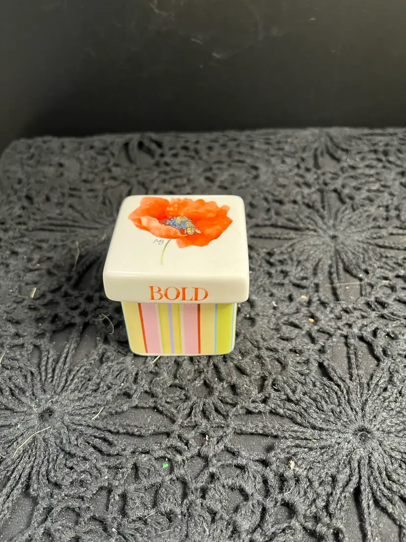 Marjolein Bastin, signed and initialed, Lidded Trinket Box. Quite colorful with Orange Poppy. Says BLOOM BOLD on the edges of the lid. On bottom inside of box "It's your day to bloom!"