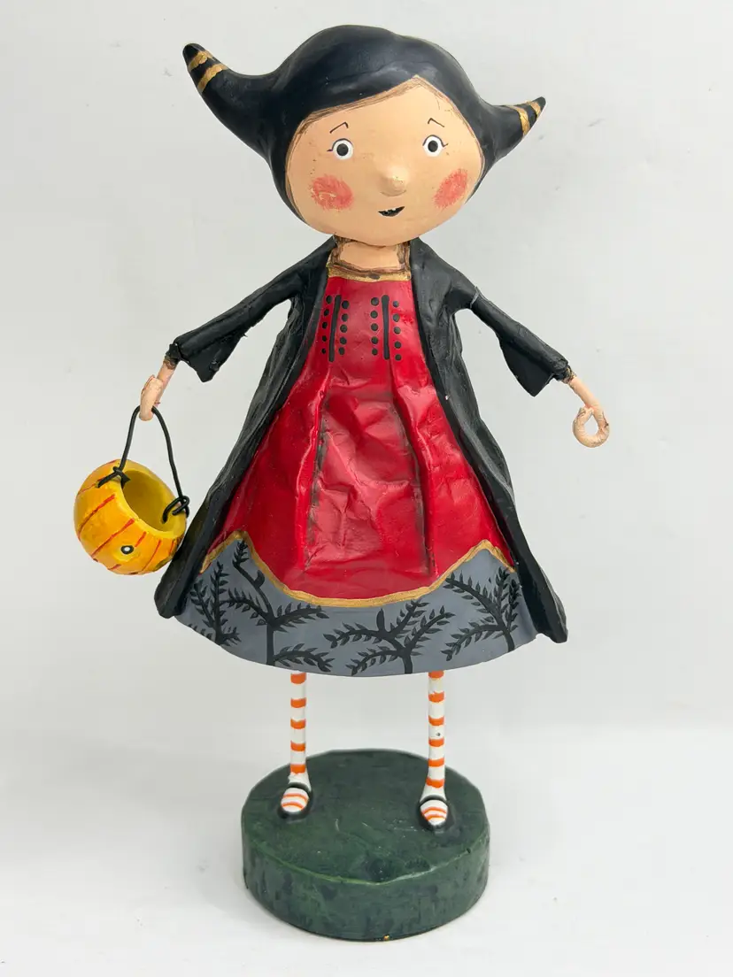 Vintage Halloween folk-art figurine designed by Lori C. Mitchell for ESC & Company. This whimsical trick-or-treat girl wears a black horned hood and flowing black coat over a bright red dress, with orange-and-white striped stockings and a hand-painted pumpkin candy bucket. The base is marked “Lori C. Mitchell © ESC,” confirming the designer and maker. Lori Mitchell is known for her nostalgic, storybook-inspired Halloween characters produced for ESC & Company.  Size: 6" high Condition: Pre-owned condition with visible age-related wear, surface marks, paint loss, and rubbing, especially around the face, costume, and base. Please review photos carefully. Era: Vintage, early 2000s SKU: XN102  Price: $49.00