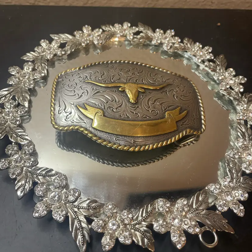 Nocona two-toned silver and gold Western-style belt buckle featuring an ornate floral engraved background, a central gold-plated longhorn steer head, an engravable ribbon banner at the bottom, and a roped edge