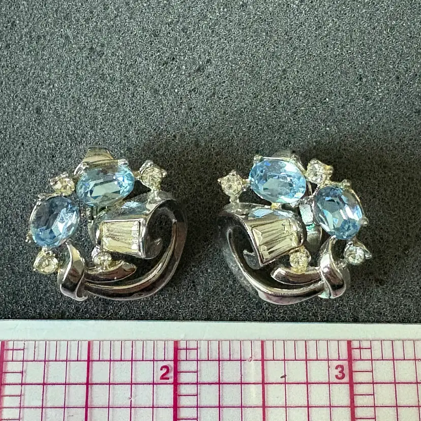 Vintage silver-tone clip-on earrings adorned with ice-blue oval crystals paired with baguette rhinestones embedded directly into the swirl. Circa late 1940s-early 1950s.