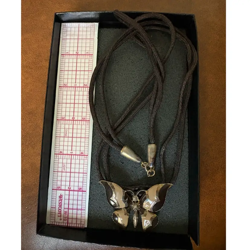 vintage gold-tone butterfly pendant necklace featuring brown and tan enameled wings with textured detailing on a dark braided cord.  Circa 1970s-1980s.