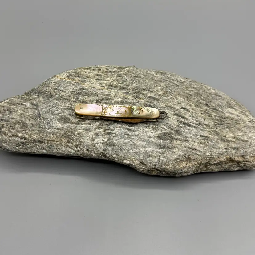 A vintage folding pen or pocket knife featuring iridescent abalone or mother-of-pearl handle