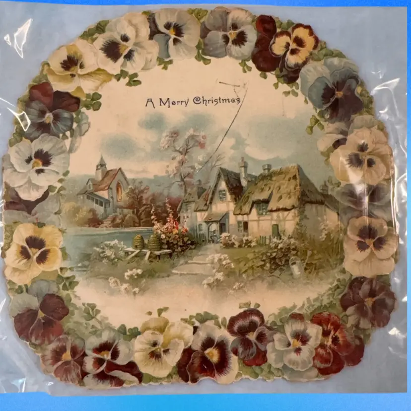 Victorian-era greeting card, a Christmas card based on the inscription.It is a die-cut design, featuring a pansy flower border surrounding a rural cottage scene. 9” Across. Please Note Pencil Writing On Back And A Mark Across Front. I Did Not Try To Remove Mark