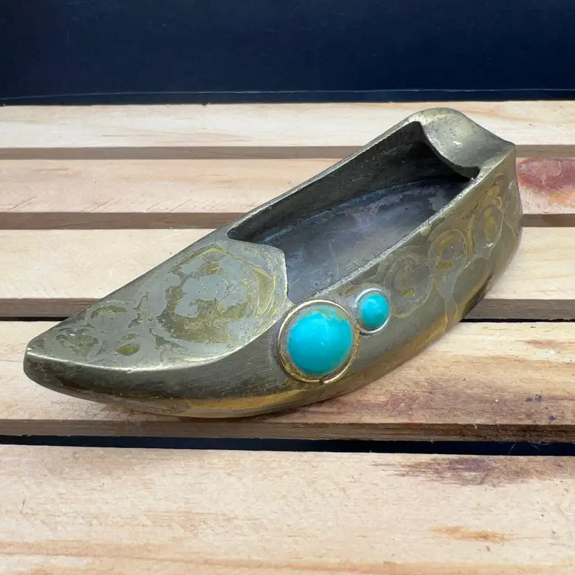 A vintage brass slipper-shaped ashtray with engraved details and stone insets.