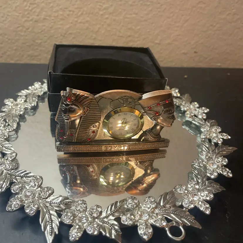 NIB Egyptian-themed desk clock featuring a miniature analog dial flanked by figures of a pharaoh and an Egyptian queen adorned with red crystal accents.