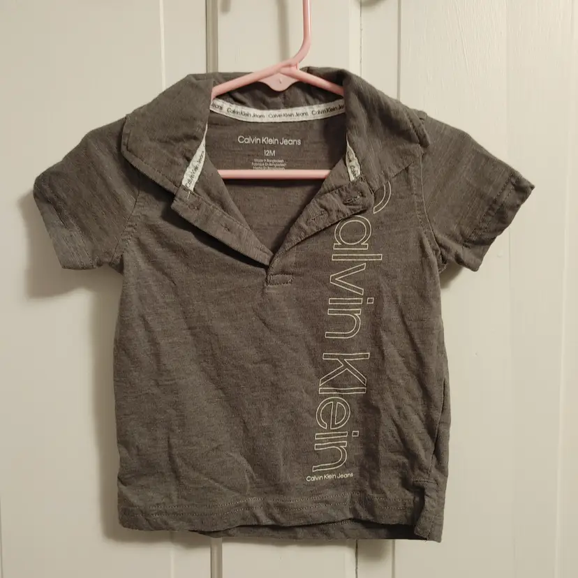 Kids- Brand: Calvin Klein Jeans. Size 12 Months. Grey shirt. Material- 60% cotton, 70% polyester. No callouts.