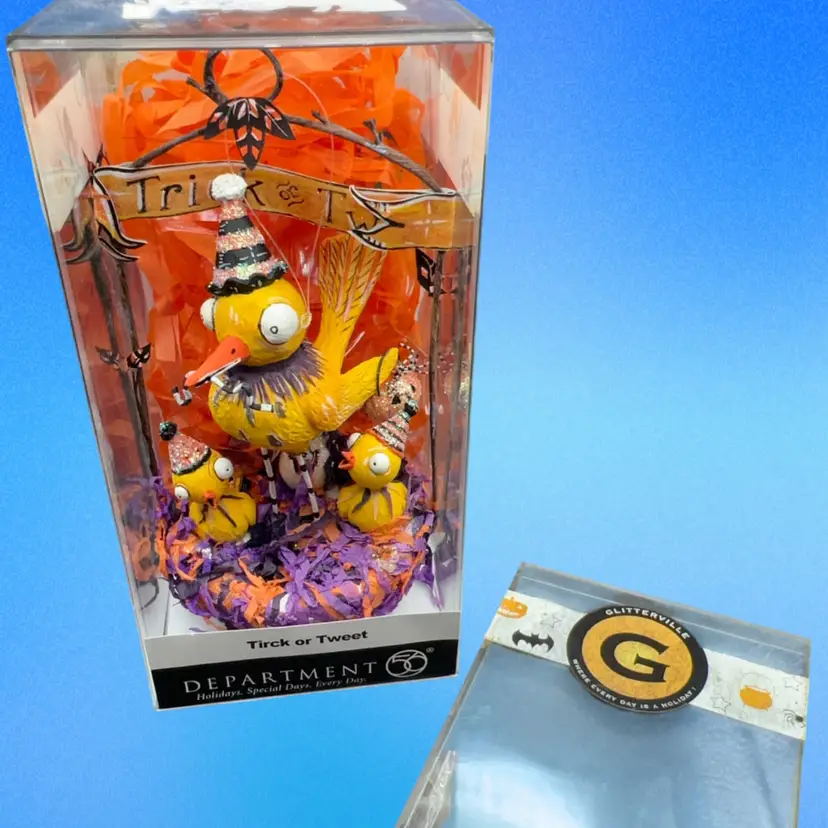 This is the Dept 56 Glitterville Halloween "Trick or Tweet" decoration, featuring a whimsical yellow bird with party hats sitting in a nest under a "Trick or Tweet" sign