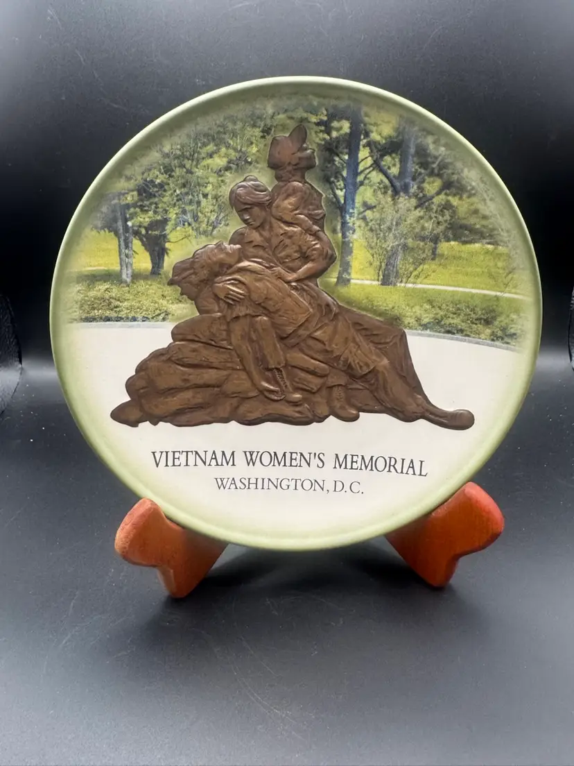 Decorative collector's plate featuring a raised, bronze-toned relief sculpture of the Vietnam Women's Memorial in Washington, D.C. 7.5” D