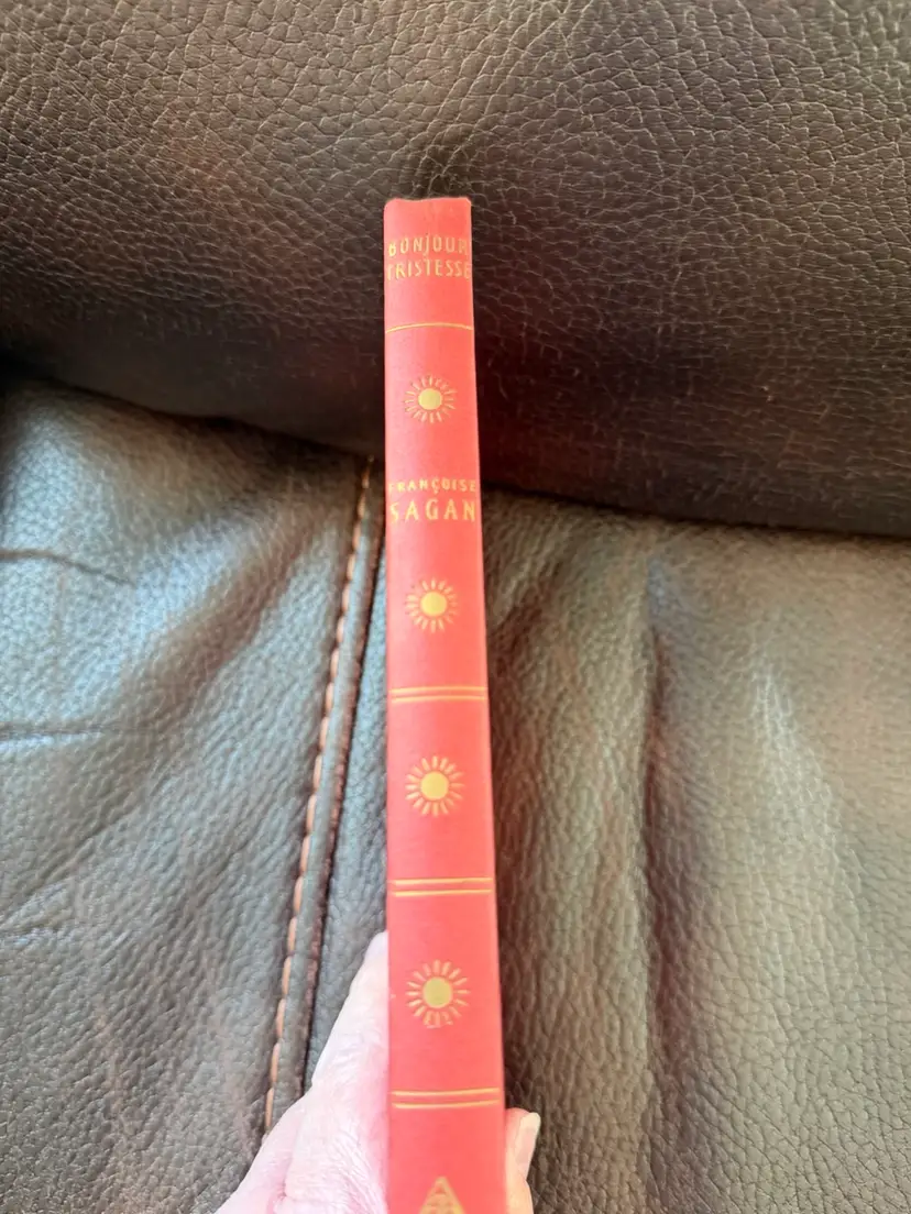 vintage red hardcover edition of Bonjour Tristesse by Françoise Sagan, featuring gold sunburst motifs along the spine.