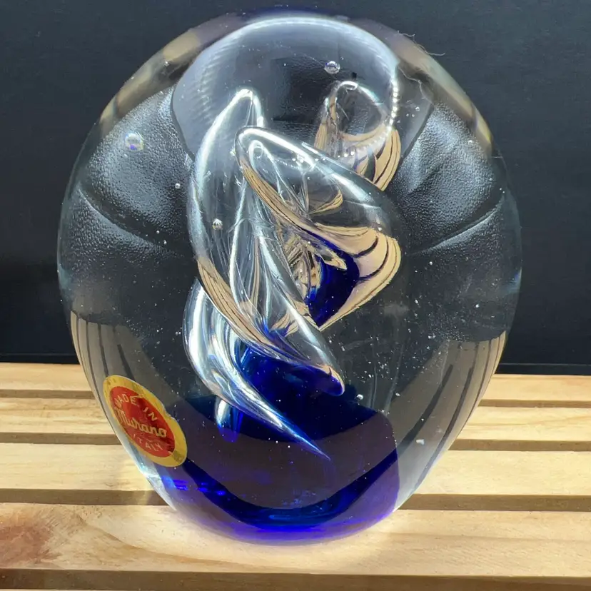 This is a Murano, cobalt blue and clear art glass egg-shaped paperweight featuring an internal swirling spiral design and a "Made in Murano Italy" sticker