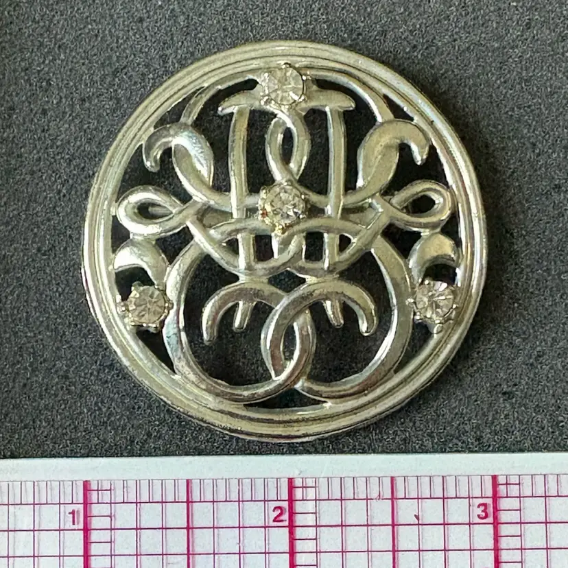 Vintage silver-tone metal filigree brooch with inlaid rhinestones and an ornate circular scroll design, 1970s-1990s.